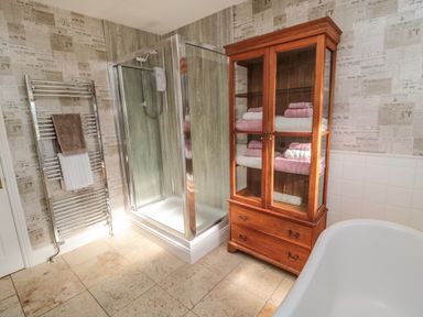 A bathroom with a glass shower enclosure metal towel rack wooden cabinet with folded towels and a bathtub at Thistleyhaugh Cottage in Longhorsley near Longframlington