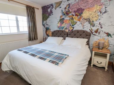 A bedroom with a large bed two bedside tables with lamps and a world map wallpaper at Thistleyhaugh Cottage in Longhorsley near Longframlington