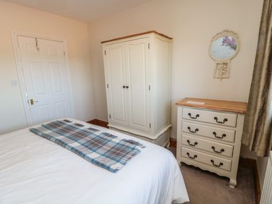A bedroom with a bed a wardrobe a chest of drawers and a wall mirror at Thistleyhaugh Cottage in Longhorsley near Longframlington