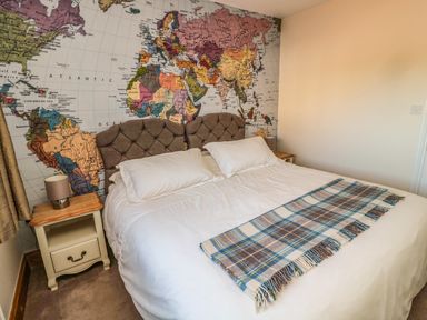 A bedroom with a double bed with white bedding and a plaid blanket at the foot of the bed with a world map wallpaper behind the headboard at Thistleyhaugh Cottage in Longhorsley near Longframlington