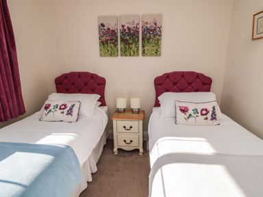 A bedroom with two single beds with purple headboards and floral cushions at Thistleyhaugh Cottage in Longhorsley near Longframlington