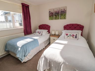 A bedroom with two single beds with pink headboards and floral cushions a bedside table with lamps and a window with curtains at Thistleyhaugh Cottage in Longhorsley near Longframlington