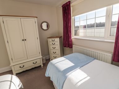 A bedroom with a bed next to a window wardrobe and chest of drawers at Thistleyhaugh Cottage in Longhorsley near Longframlington