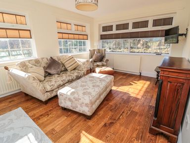A sitting room with floral sofa armchair ottoman wooden floor and television at Thistleyhaugh Cottage in Longhorsley near Longframlington