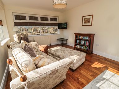 A sitting room with a floral sofa and ottoman a wooden bookshelf and a wall mounted TV at Thistleyhaugh Cottage in Longhorsley near Longframlington