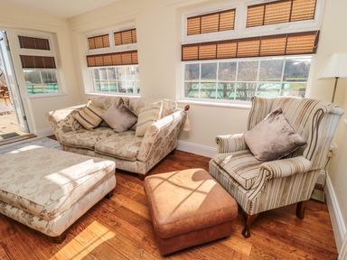 A sitting area with a floral sofa ottoman striped armchair and brown ottoman near windows in a room at Thistleyhaugh Cottage in Longhorsley near Longframlington