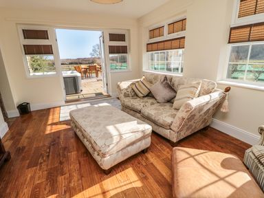 A sitting room with floral patterned sofa padded ottoman and wooden floor with doors opening to outdoor patio at Thistleyhaugh Cottage in Longhorsley near Longframlington