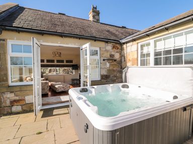 An outdoor hot tub on a stone patio next to an open door leading to a living room at Thistleyhaugh Cottage in Longhorsley near Longframlington