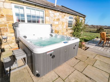 An outdoor hot tub with steps beside a stone house and a wooden deck with chairs and table at Thistleyhaugh Cottage in Longhorsley near Longframlington