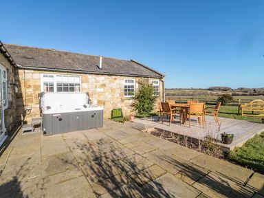 An outdoor patio area with a hot tub wooden table and chairs a bench and stone house with windows at Thistleyhaugh Cottage Longhorsley near Longframlington