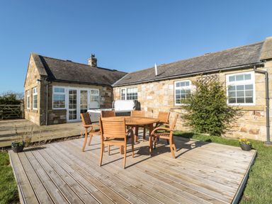 An outdoor wooden deck with a round table and six chairs next to a stone house at Thistleyhaugh Cottage in Longhorsley near Longframlington
