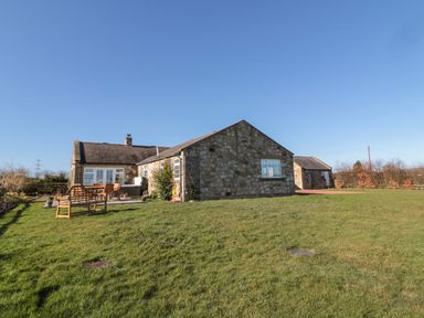 A stone cottage with outdoor seating and lawn at Thistleyhaugh Cottage in Longhorsley near Longframlington