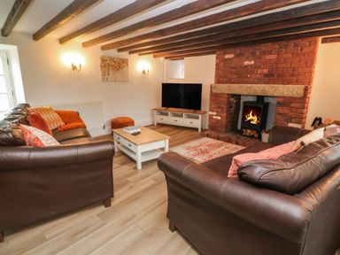 A living room with leather sofas a coffee table a television and a fireplace at Trevedran Cottage in St Buryan