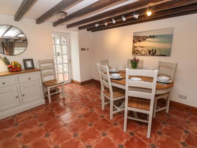 A dining room with a wooden table set for six chairs and a buffet with fruit at Trevedran Cottage in St Buryan