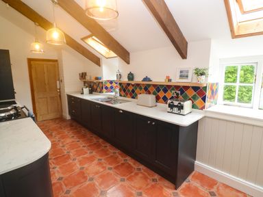 A kitchen with dark cabinets white countertops colorful tiled backsplash and terracotta floor at Trevedran Cottage in St Buryan