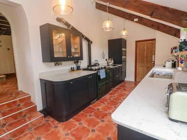 A kitchen with black cabinets white countertops a stove and terracotta tiled floor at Trevedran Cottage in St Buryan