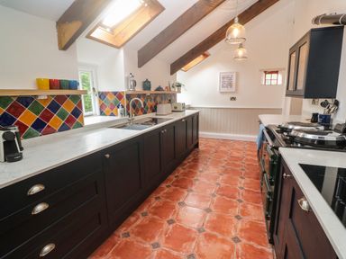 A kitchen with dark cabinets colorful tiled backsplash skylights and terracotta floor tiles at Trevedran Cottage in St Buryan