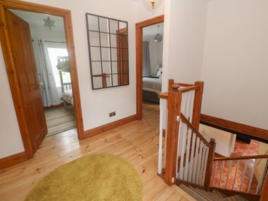 A hallway with wooden floors a round rug a staircase and doorways leading to two bedrooms at Trevedran Cottage in St Buryan