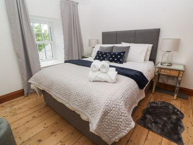 A bedroom with a bed with pillows and folded towels two bedside tables with lamps and curtains on a window at Trevedran Cottage in St Buryan