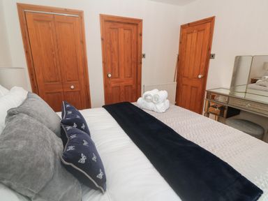 A bedroom with a bed with pillows and rolled towels three wooden doors and a mirror vanity table at Trevedran Cottage in St Buryan