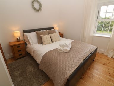 A bedroom with a double bed wooden bedside tables lamps and a window at Trevedran Cottage in St Buryan