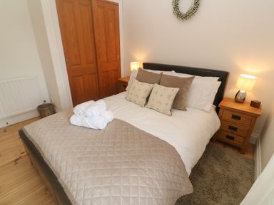 A bedroom with a bed with pillows and folded towels next to wooden nightstands with lamps at Trevedran Cottage in St Buryan