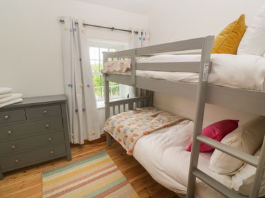 A bedroom with a gray bunk bed a gray chest of drawers and a multicolored rug at Trevedran Cottage in St Buryan