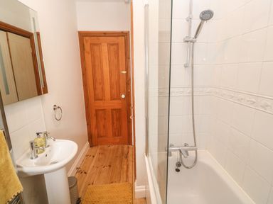 A bathroom with a wooden door a sink with soap a bathtub with a shower and a yellow rug at Trevedran Cottage in St Buryan
