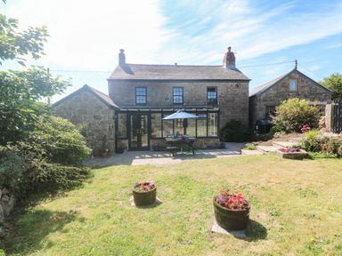A stone cottage with a patio table and umbrella in a garden with two flower pots at Trevedran Cottage in St Buryan