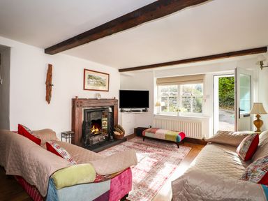 A living room with two sofas a fireplace a television a window and an open door at Bay Tree Cottage in Ambleside
