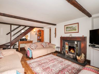 A living room with sofas a fireplace wooden beams a rug and a television at Bay Tree Cottage in Ambleside
