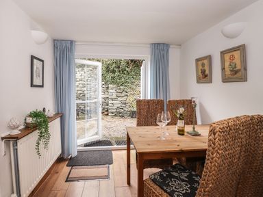 A dining area with a wooden table and woven chairs next to open glass doors leading to a stone patio at Bay Tree Cottage Ambleside