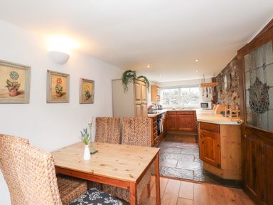 A kitchen with wooden cabinets and dining table with woven chairs at Bay Tree Cottage in Ambleside