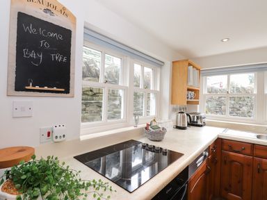 A kitchen with wooden cabinets a black stovetop a basket with tea bags a kettle and a toaster on the counter at Bay Tree Cottage Ambleside