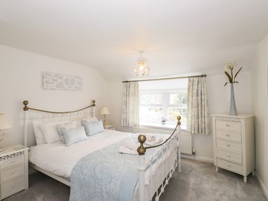 A bedroom with a bed with patterned bedding two bedside tables with lamps a window with curtains and a chest of drawers with a vase at Bay Tree Cottage Ambleside