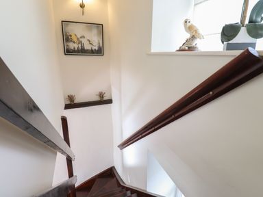 A staircase with dark wooden handrails and steps with a painting and plants on a shelf at Bay Tree Cottage Ambleside