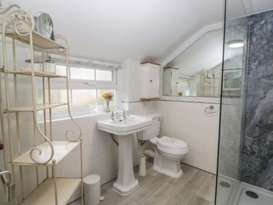 A bathroom with a sink, toilet, shower, and shelf at Bay Tree Cottage in Ambleside