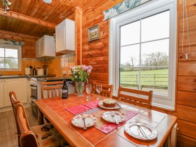 A kitchen and dining area with a wooden table set for three and a window overlooking a field at Orchard Lodge in Hockworthy near Sampford Peverell Devon