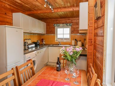 A kitchen with wooden walls and ceiling a tiled table with flowers and glasses and white cabinets at Orchard Lodge in Hockworthy near Sampford Peverell Devon