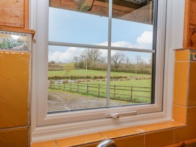 A view of a green field with a wooden fence and trees through a kitchen window with yellow tiles at Orchard Lodge in Hockworthy near Sampford Peverell Devon