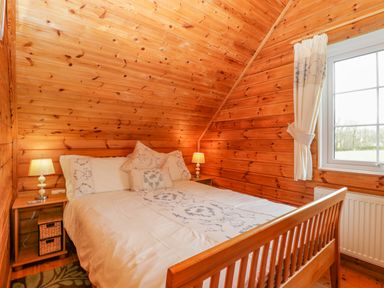 A bedroom with wood panel walls a bed with white bedding two bedside tables with lamps and a window with curtains at Orchard Lodge in Hockworthy near Sampford Peverell Devon