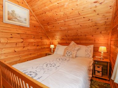 A bedroom with wooden walls and ceiling a bed with white decorated bedding and two bedside tables with lamps at Orchard Lodge in Hockworthy near Sampford Peverell Devon