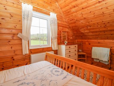 A bedroom with wooden walls a bed a window with curtains a chest of drawers a chair and a towel rack at Orchard Lodge in Hockworthy near Sampford Peverell Devon