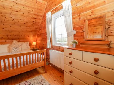 A bedroom with a wooden bed a chest of drawers with a mirror and a window with curtains at Orchard Lodge in Hockworthy near Sampford Peverell Devon