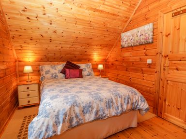 A bedroom with a double bed and two bedside tables with lamps in a wooden room at Orchard Lodge Hockworthy near Sampford Peverell Devon