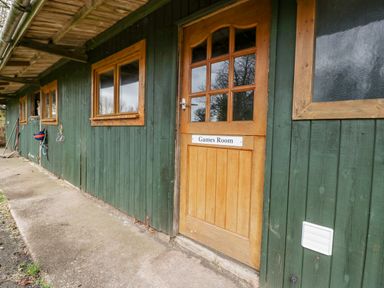 An exterior corridor with a wooden door labeled Games Room and green wooden walls at Orchard Lodge in Hockworthy near Sampford Peverell Devon