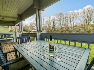 A covered wooden porch with a table holding a bottle of wine and two wine glasses at Orchard Lodge in Hockworthy near Sampford Peverell Devon