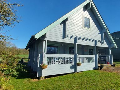 A wooden house with a porch and hanging baskets on grass at Orchard Lodge in Hockworthy near Sampford Peverell Devon