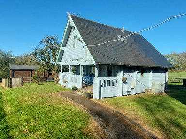 A light blue wooden house with a black roof on a grass lawn at Orchard Lodge in Hockworthy near Sampford Peverell Devon