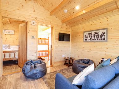 A wooden living room with blue sofa bean bags wall mounted tv and framed cow picture at Clover Lodge in Theberton near Leiston